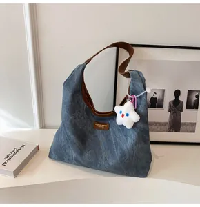 Detail of blue canvas hobo bag with leather strap, logo patch and star plush charm
