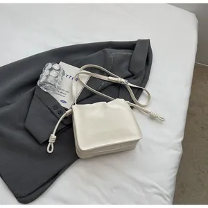 Detail view of cream white pleated shoulder bag with unique side knot on a gray suit