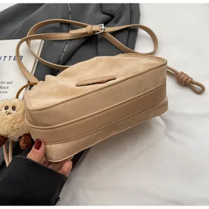 Detail of khaki pleated crossbody bag featuring matte texture and cute plush charm pendant