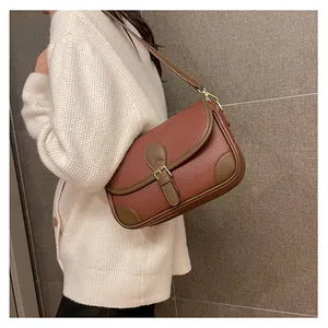 Close-up of saddle bag with red litchi texture and brown trim worn with cream sweater