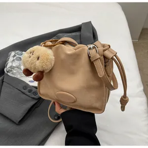Detail of beige pleated crossbody bag with matte texture and decorative plush pendant