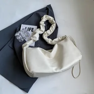 Minimalist cream shoulder bag with pleated strap on grey blazer for a modern aesthetic