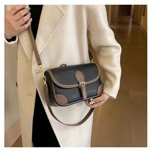 Classic black leather crossbody bag with brown trim shown on a model in a warm hallway