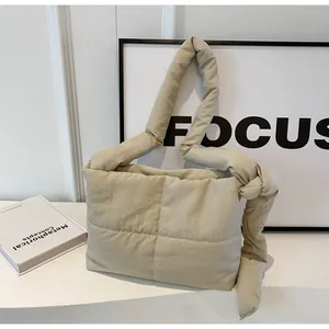 Close-up of beige quilted puffy shoulder bag with knotted strap in a minimalist setting