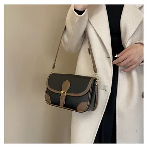 Detail of crossbody bag in black pebble leather with brown trim and gold buckle