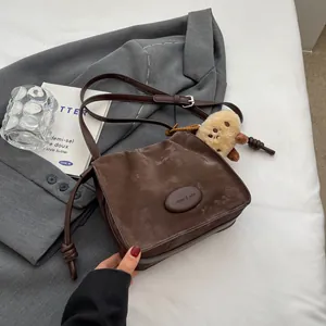 Deep brown pleated retro hobo bag with plush pendant on a grey suit background