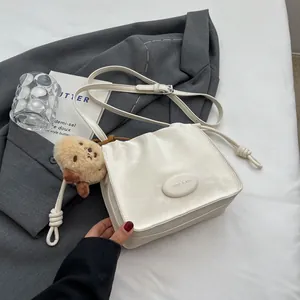 Minimalist beige pleated crossbody bucket bag with cute plush dog pendant on a jacket