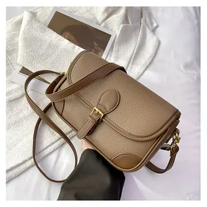 Detailed close-up of brown pebbled leather texture and golden metal buckle on crossbody bag