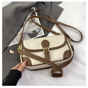 Close-up of retro cream leather crossbody bag with brown trim and gold metal buckles