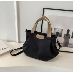 Detail of black canvas tote bag showing the brown leather logo and adjustable shoulder strap