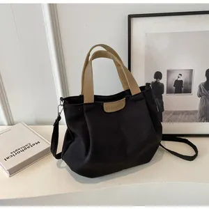 Detail of black canvas tote bag showing the leather logo patch and detachable strap