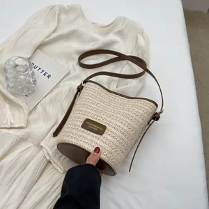 Straw woven bucket bag with brown leather trim and shoulder strap on white dress background