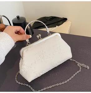 Dettaglio dell'elegante borsa da sera in pizzo beige con ricamo floreale e chiusura a scatto