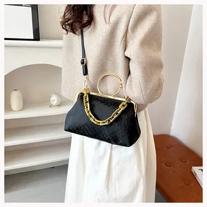 Detail of black patterned fabric evening bag with chunky gold chain and ring handle