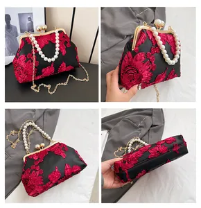 Detail of vintage lace evening bag featuring red floral embroidery and pearl handle