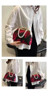 Detail of vintage lace bag with red floral embroidery, pearl handle, and metal chain strap