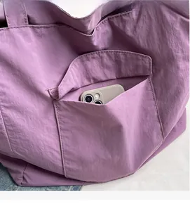 Macro detail of purple nylon tote bag front pocket showing spacious storage for a smartphone