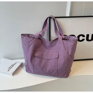 Detailed view of purple nylon tote bag with large front pocket on a modern white stand