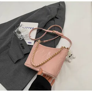 Roze bucket bag met marmertextuur, goudkleurige ketting en pluche hanger op grijs jasje