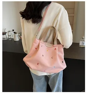 Detail of pink canvas tote with colorful embroidered letters and brand label on strap