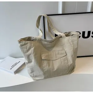 Close-up of beige nylon tote bag with functional flap pocket and durable top handles