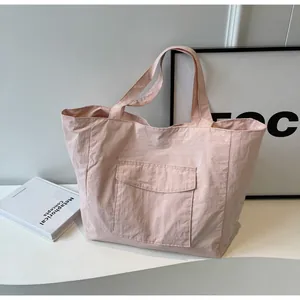 Detail of light pink nylon tote bag showing textured fabric and front pocket design