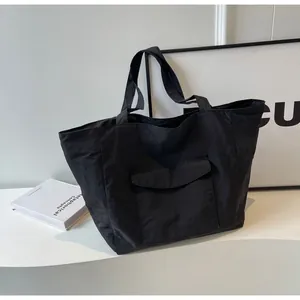 Detail of black nylon tote bag featuring front flap pocket and minimalist aesthetic