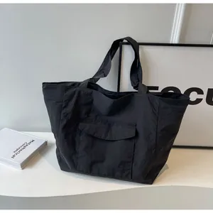 Detail of black nylon tote bag featuring front flap pocket and lightweight texture