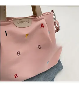Detail of pink canvas tote showing colorful letter embroidery and faux leather logo patch
