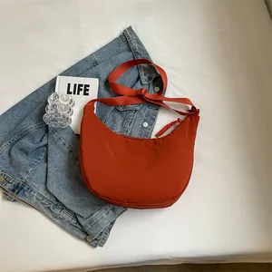 Sac bandoulière demi-lune rouge rouille en nylon posé sur une veste en jean bleu