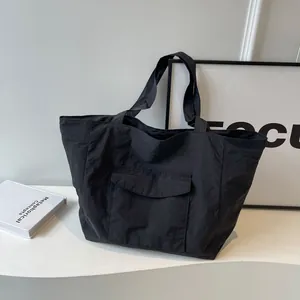 Minimalist black nylon tote bag with front pocket shown in a modern urban setting