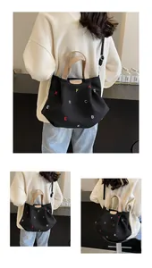 Detailed view of black canvas tote bag featuring vibrant colorful letter embroidery and leather handles