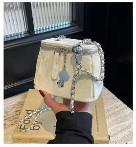 Gros plan du sac seau crème avec breloque camélia et bandoulière chaîne argent