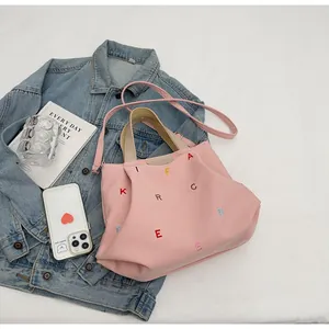 Detail of pink canvas tote bag featuring vibrant letter embroidery and leather logo patch