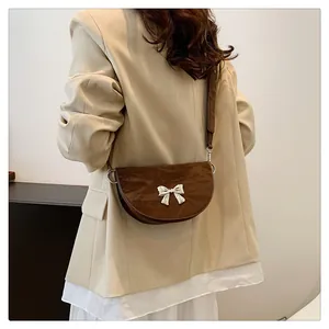 Détail du sac selle marron foncé avec boucle nœud argentée sur un modèle en blazer beige