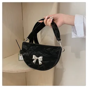 Détail du sac demi-lune plissé noir avec un nœud en métal argenté et une finition brillante