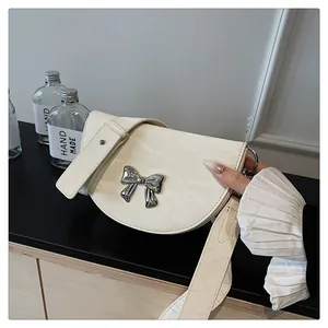 Détail d'un sac bandoulière demi-lune crème avec un ornement de nœud argenté brillant
