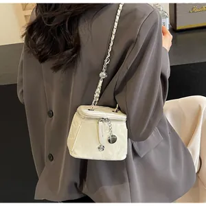 Détail du sac bandoulière blanc avec pendentif camélia porté sur un costume gris