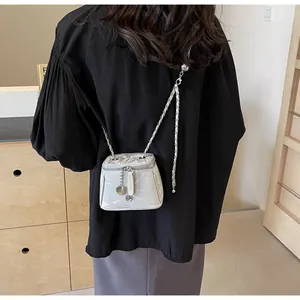Détail du sac seau argenté avec bandoulière chaîne et breloque camélia au fini métal