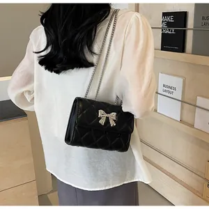 Détail d'un sac bandoulière matelassé noir avec boucle nœud en métal argenté sur un mannequin