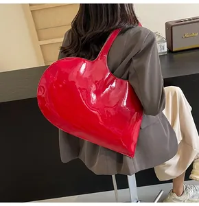 Model wearing a large red heart-shaped patent leather shoulder bag with glossy finish