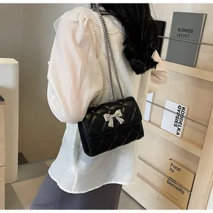 Détail d'un sac à bandoulière en cuir matelassé noir avec nœud argenté et bandoulière chaîne