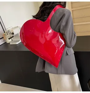 Detail of red heart-shaped shoulder bag with glossy patent finish worn by model in a cafe
