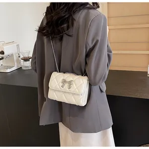 Détail d'un sac bandoulière matelassé crème avec nœud argenté et bandoulière chaîne