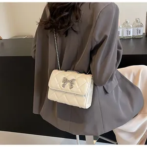 Sac à bandoulière matelassé avec nœud argenté, porté sur l'épaule contre un blazer gris