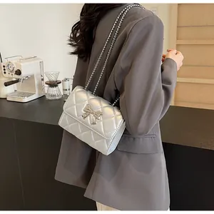 Sac bandoulière argenté matelassé avec nœud métallique porté par un mannequin
