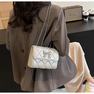 Détail d'un sac bandoulière argenté matelassé avec nœud décoratif et chaîne en métal