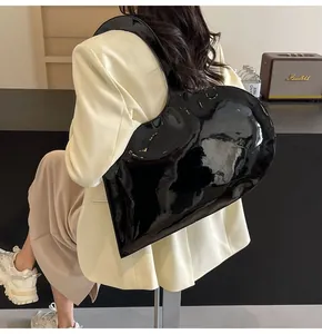 Glossy black heart-shaped shoulder bag shown on model in a stylish office setting