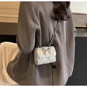 Détail d'un sac bandoulière argenté matelassé avec nœud métallique et fine bandoulière