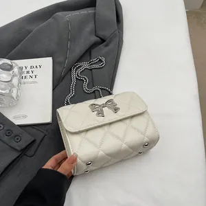 Sac bandoulière matelassé blanc avec nœud argenté et chaîne sur un décor élégant